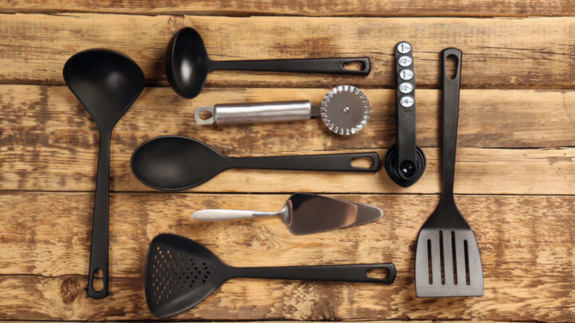 A variety of kitchen utensils arranged on a wooden table, including spoons, spatulas, and measuring cups.