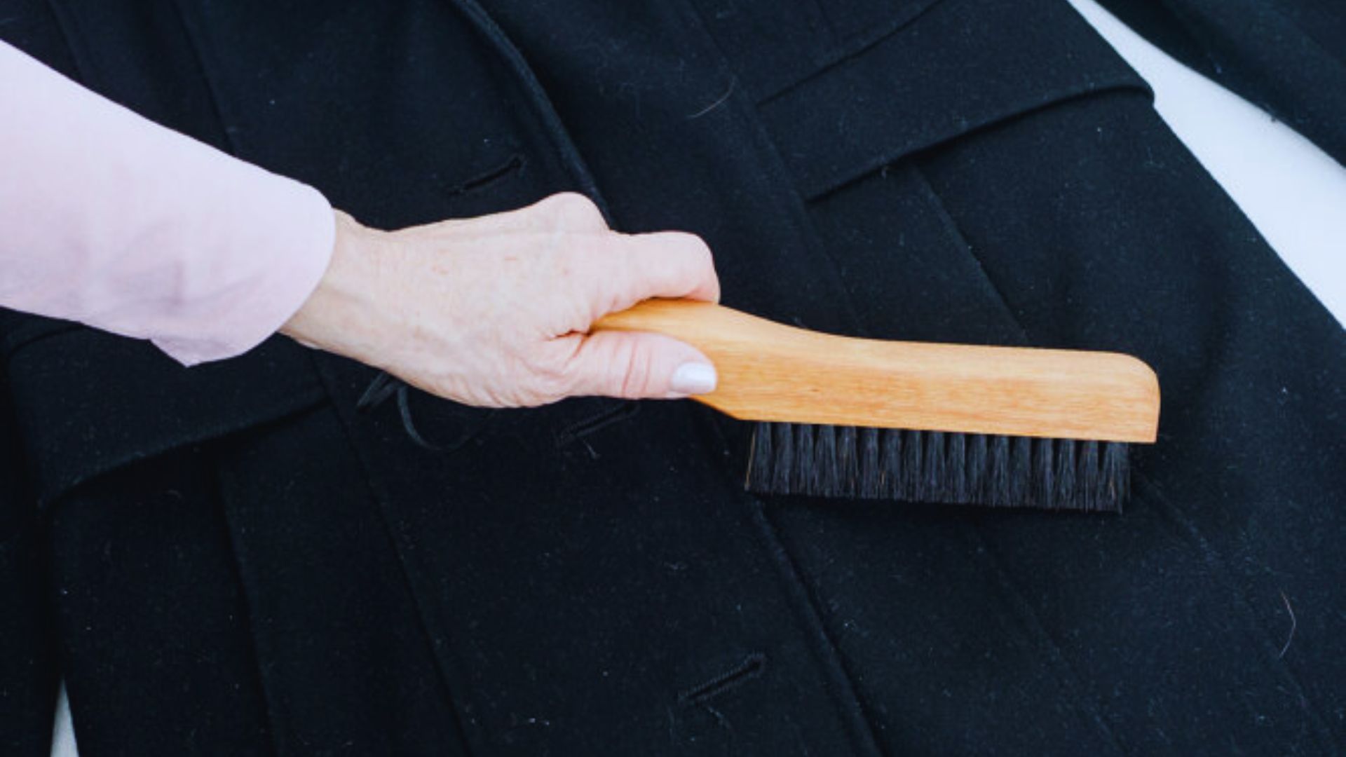 A person brushes a black coat with a wooden brush, focusing on maintaining its appearance and texture.