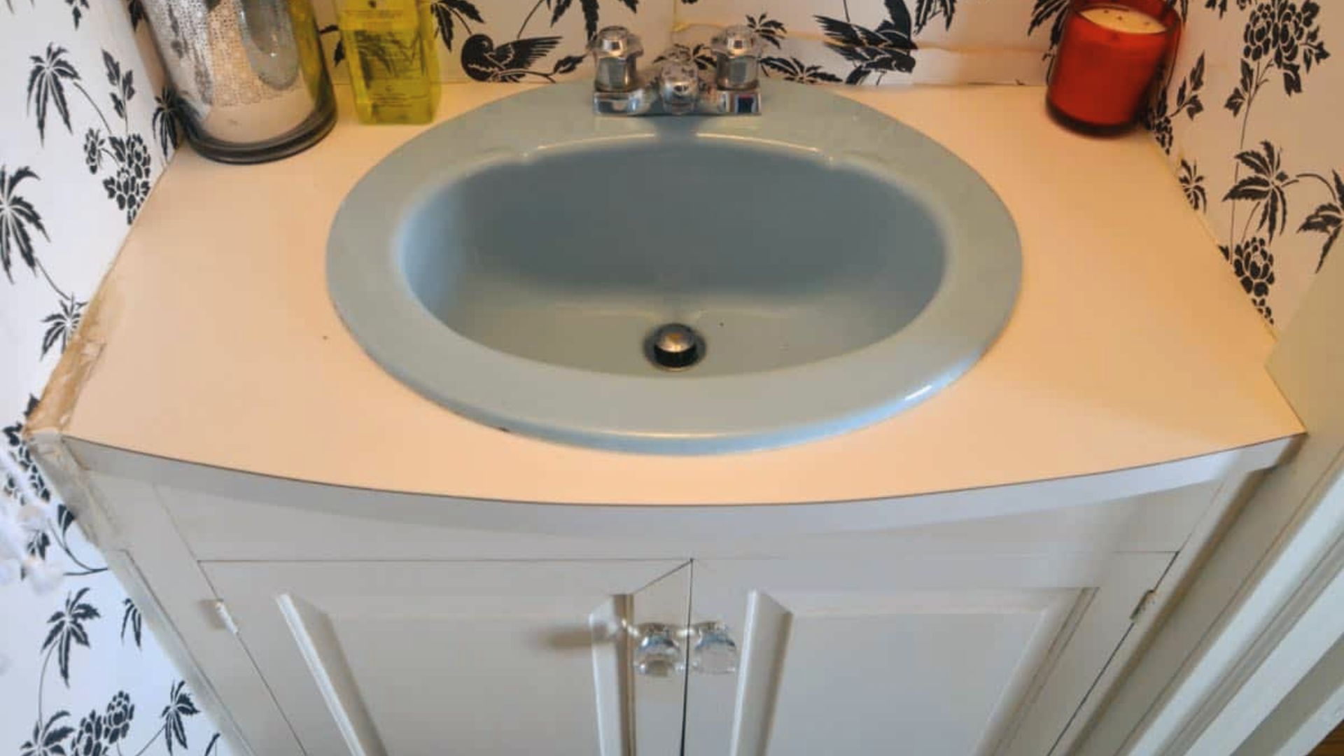Dated vanity with light blue sink and white base showing before refinishing condition and wear.