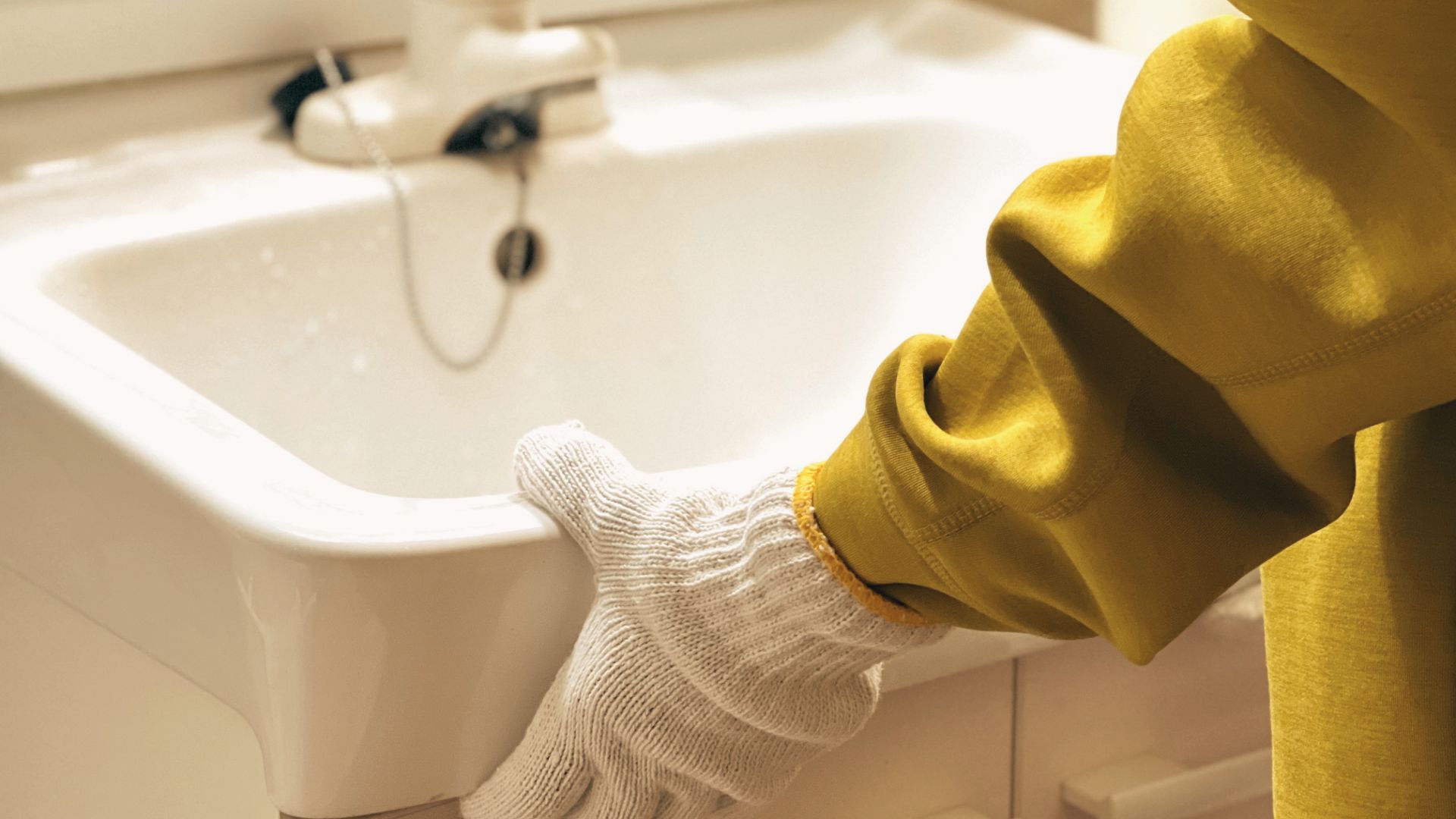 Close-up of gloved hand holding white sink edge during vanity removal or refinishing process.