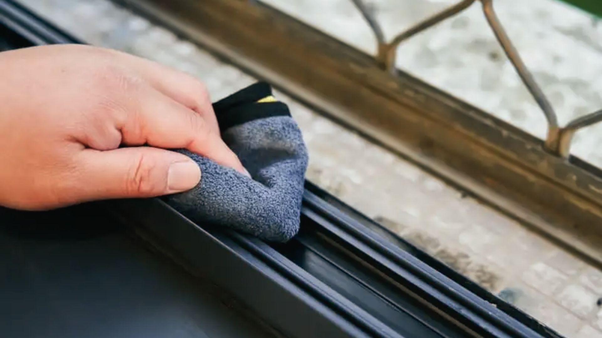 Hand wiping window track corners with a microfiber cloth to remove loosened dirt and residue.