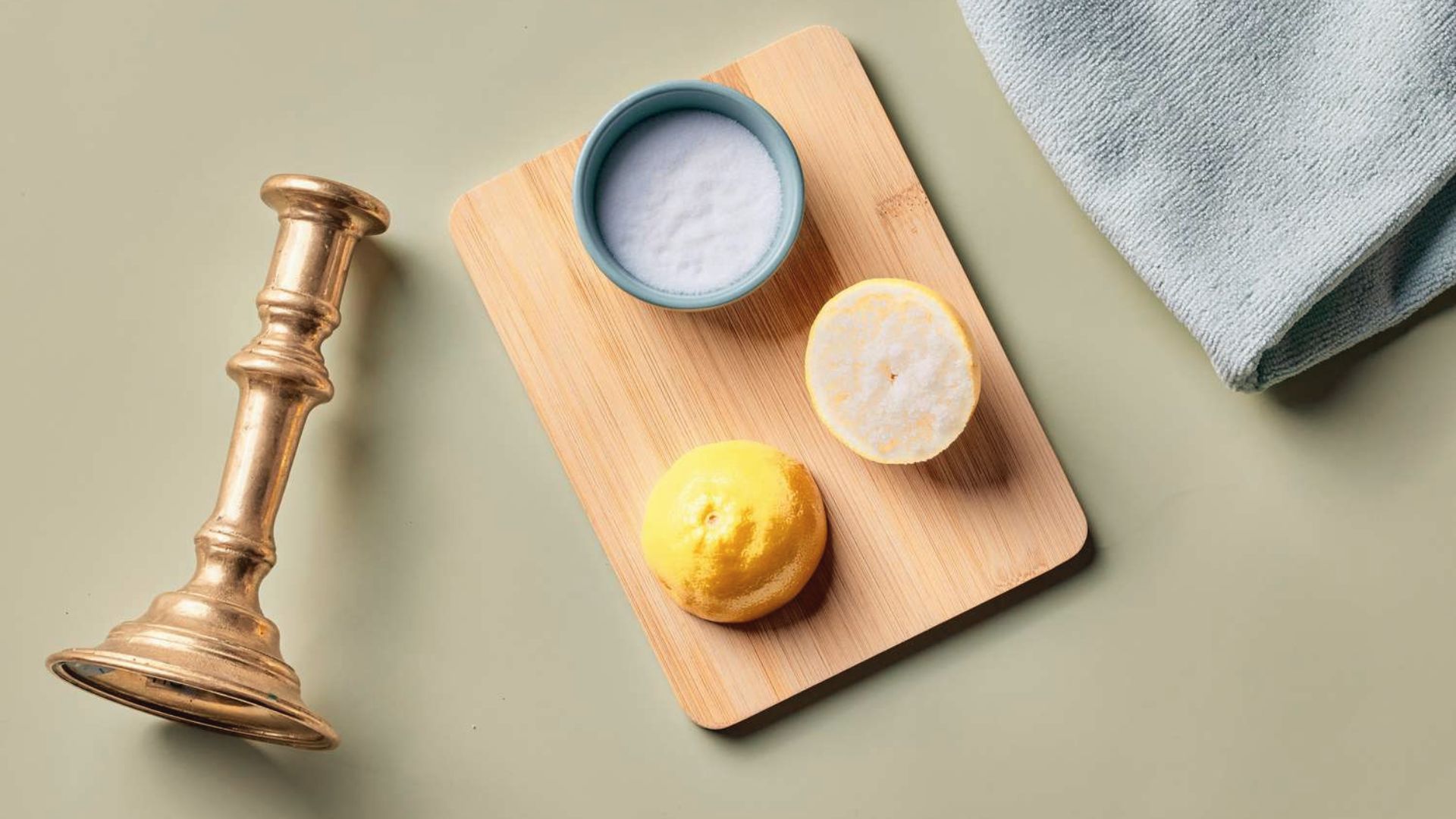 Lemon halves, salt bowl, and brass candlestick arranged on board as natural brass cleaning supplies.