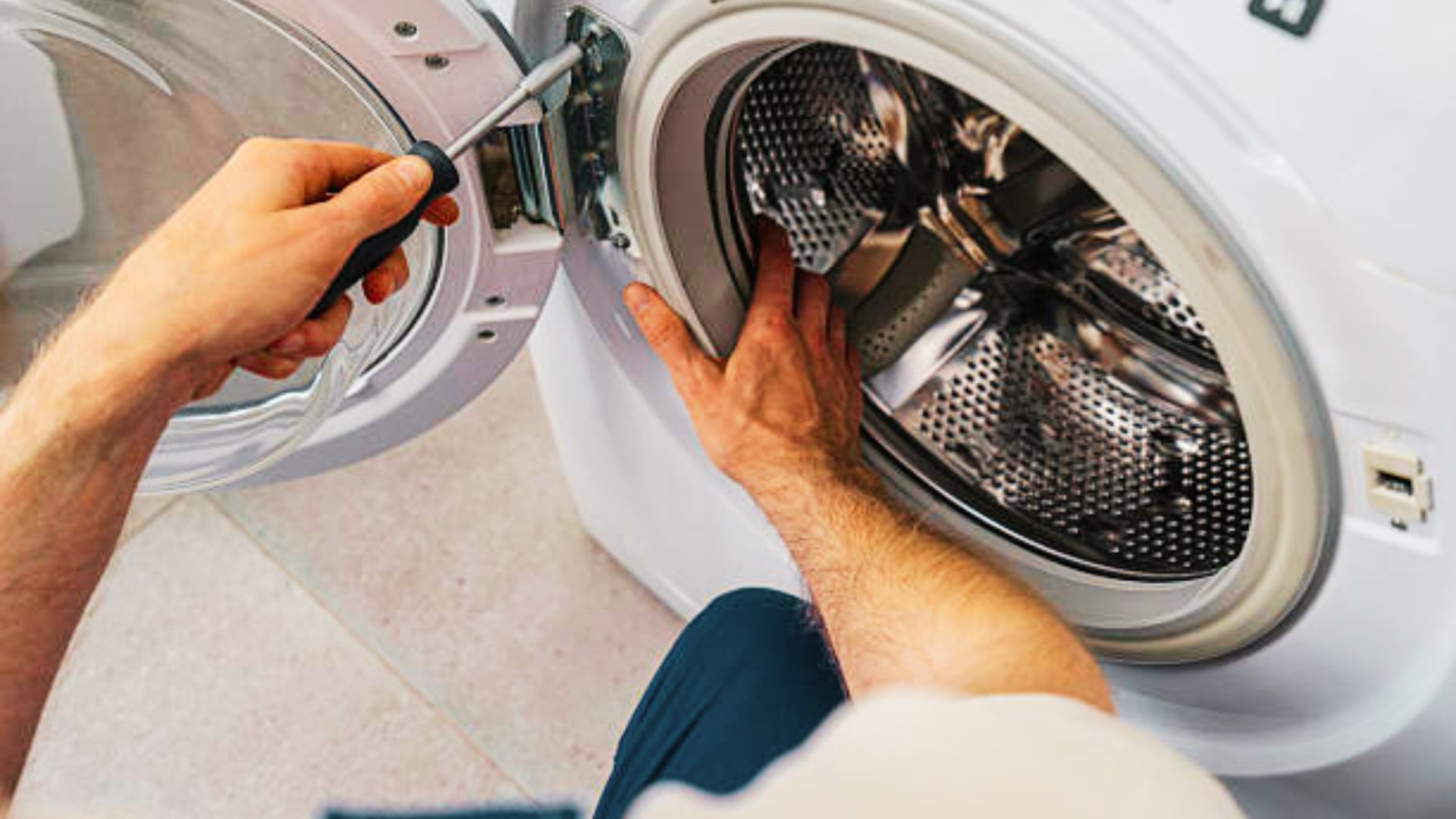 Appliance technician fixing squeaky washing machine with screwdriver.