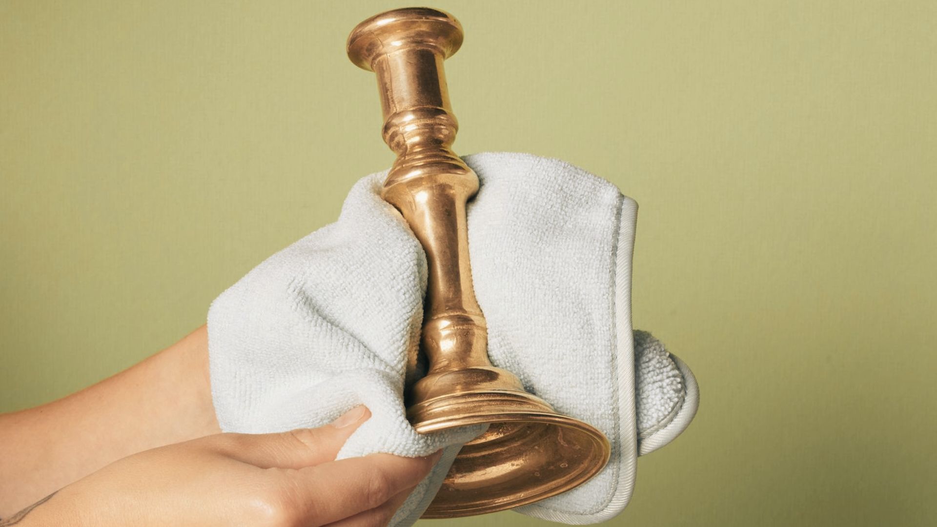 Hands drying a polished brass candlestick with a white cloth to prevent water spots and add shine.