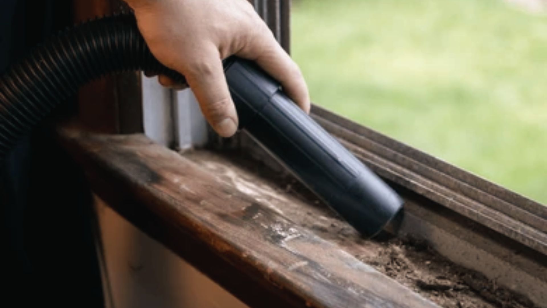 Person vacuuming loose debris from window track with hose attachment for deep cleaning.