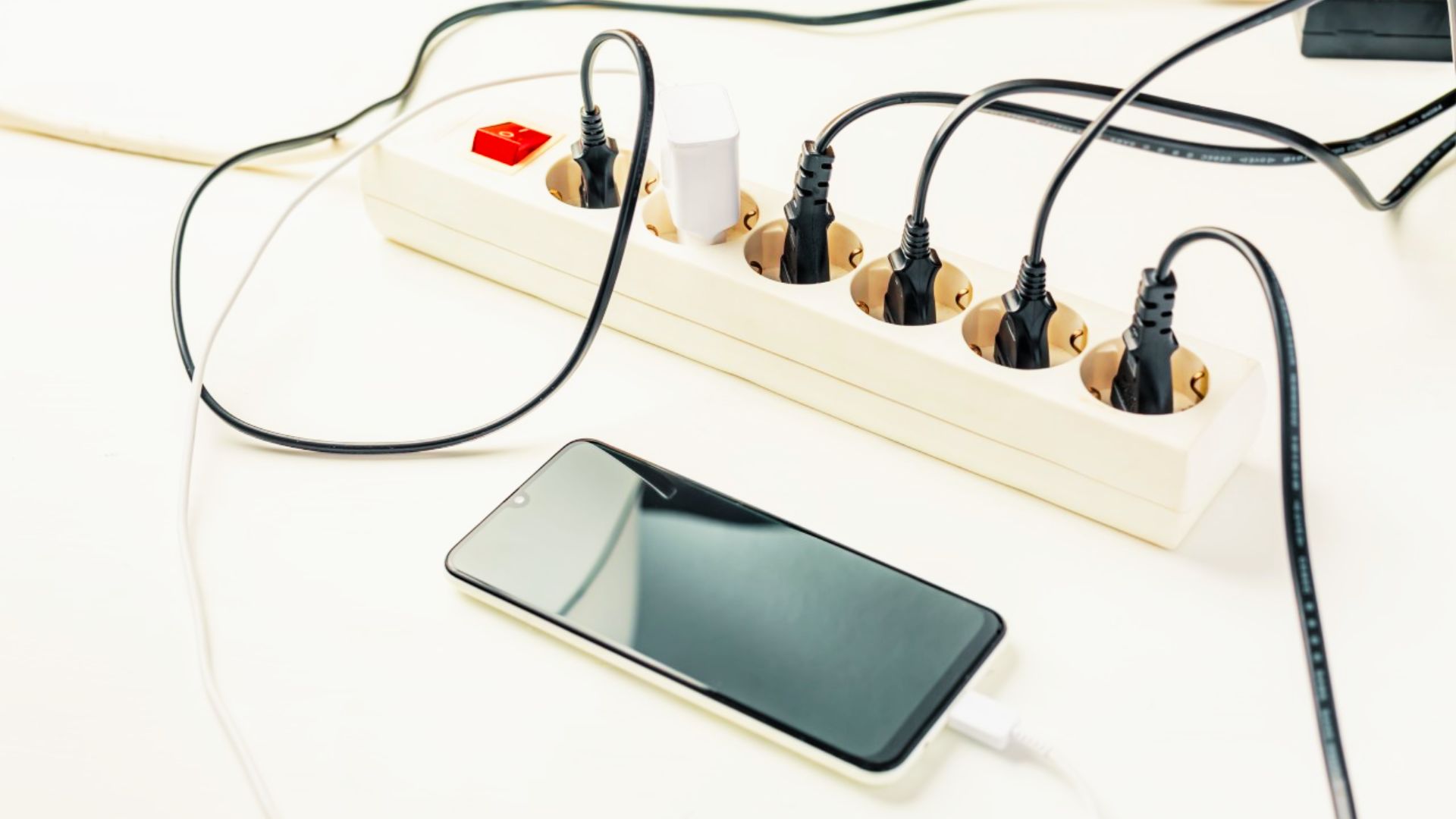 Power strip with multiple device plugs and a charging smartphone showing sources of vampire energy drain.