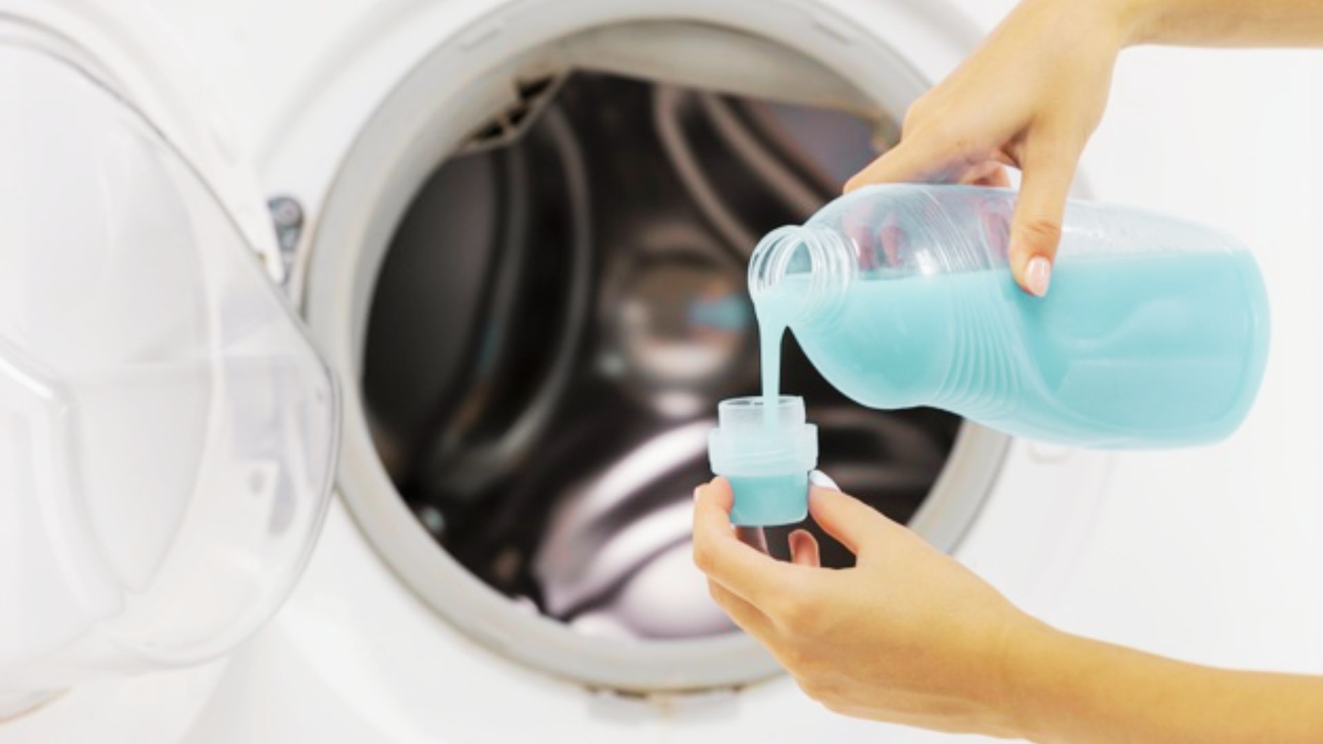 Person pouring blue detergent into a cap before a front-load washer for a sanitized wash cycle.