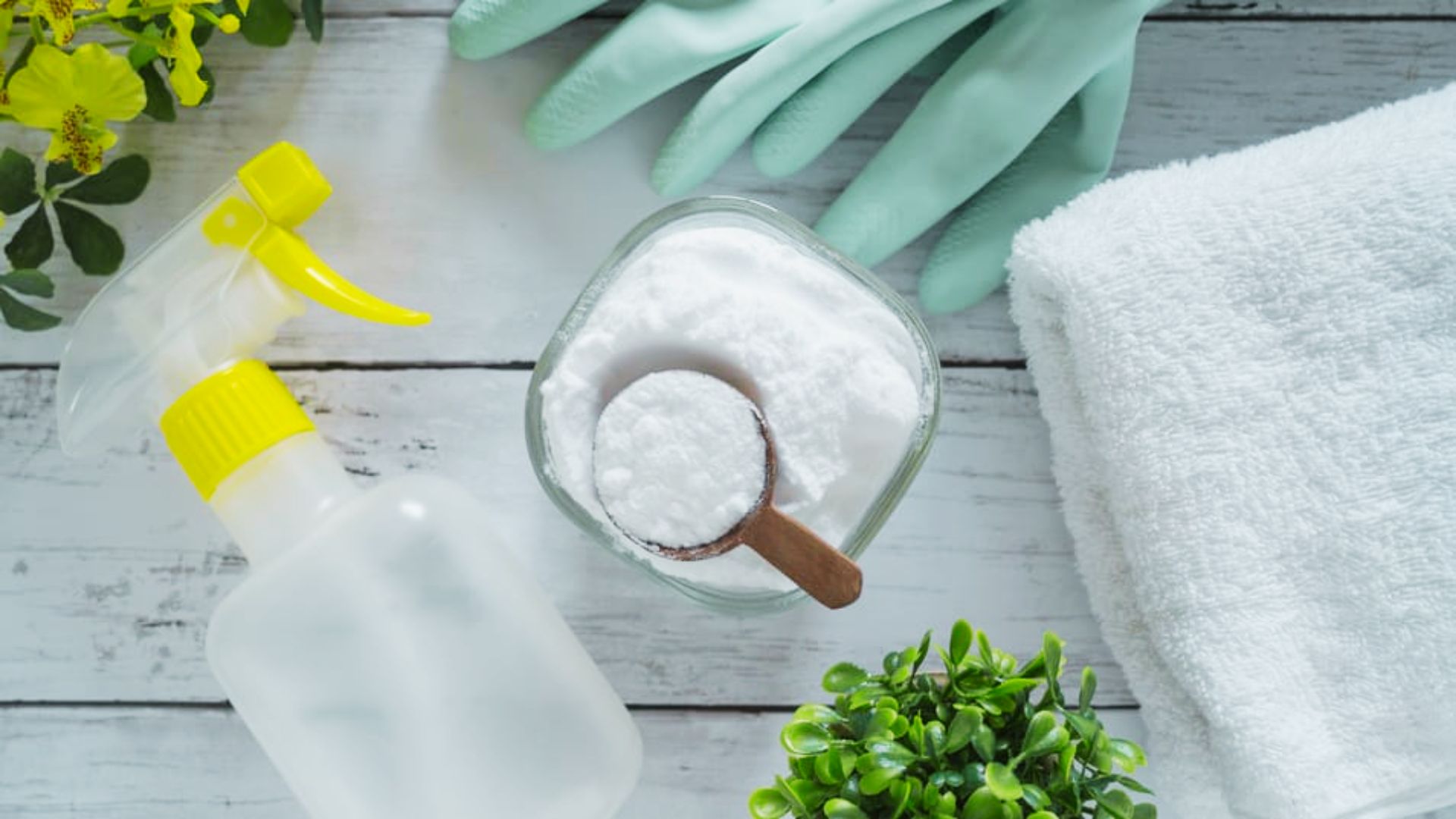 A bowl of baking soda, spray bottle, rubber gloves, and towel laid on a wooden surface