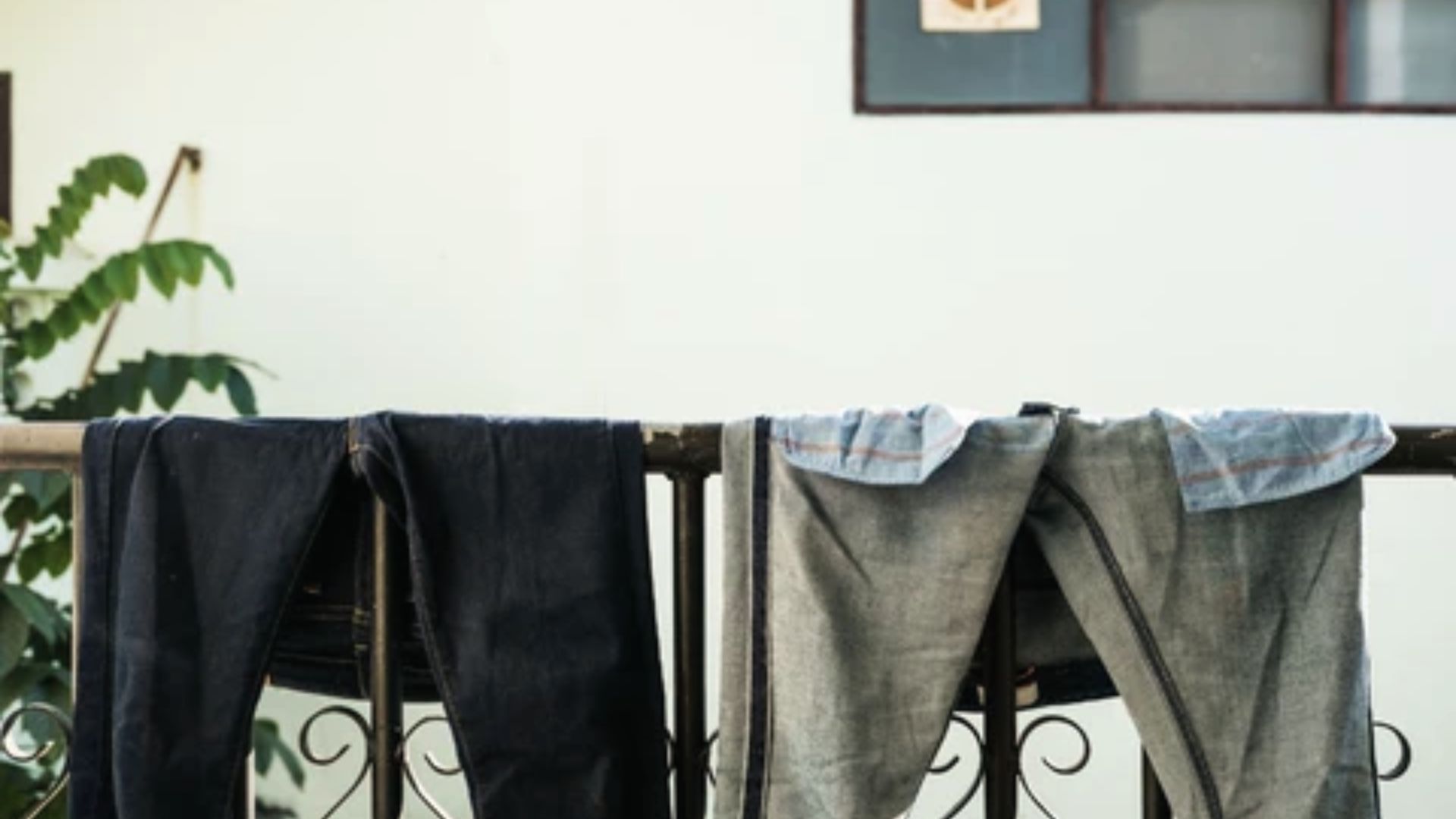 Black jeans and other clothes hang on a balcony railing to air dry in the shade.