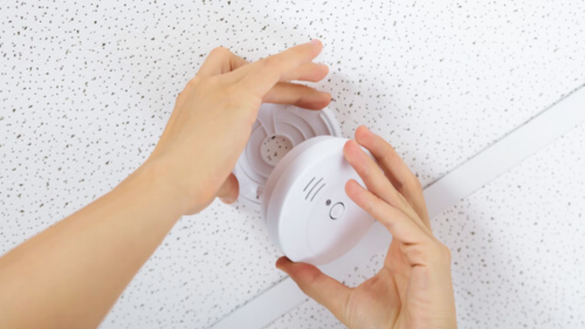 Hands install ceiling smoke detector for fire safety and early hazard detection at home