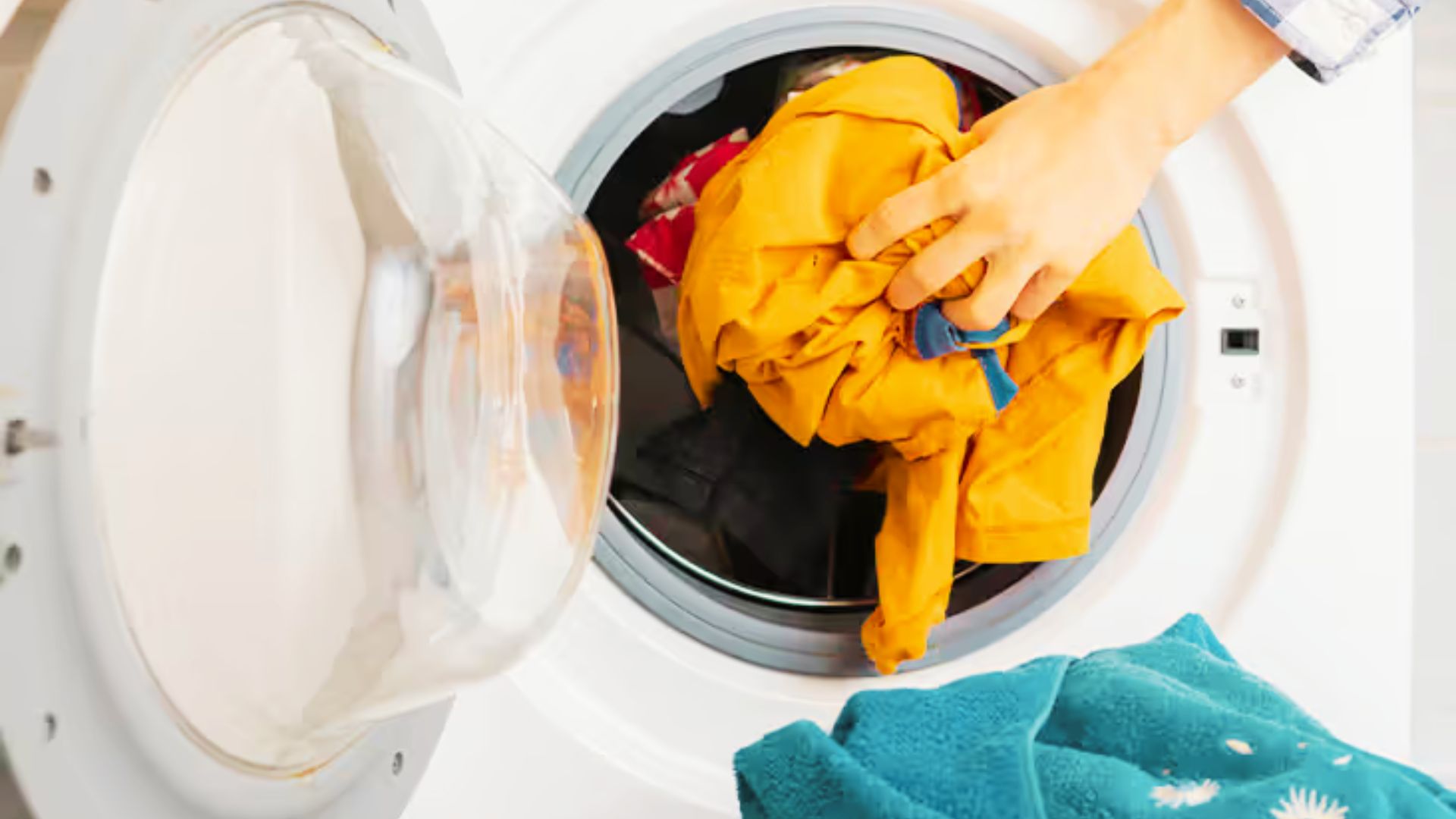 A person pulls a yellow garment from a front-load washing machine with other damp clothes inside.