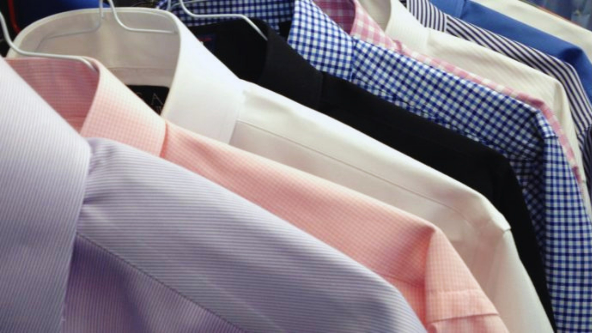 Row of crisp dress shirts in pink, white, and blue checks hanging on white hangers in bright store lighting