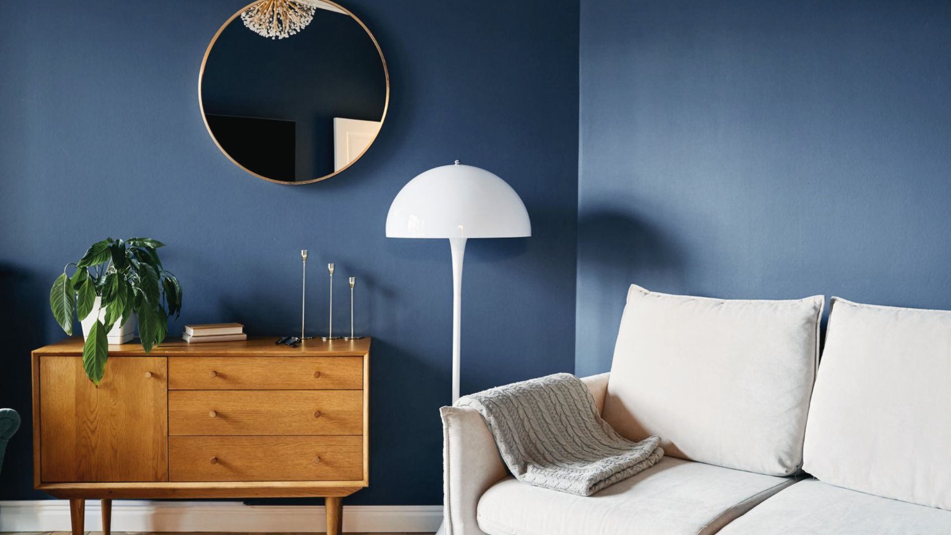 Add drama on a budget with deep navy walls, gold round mirror, and thrifted mid-century wood console.