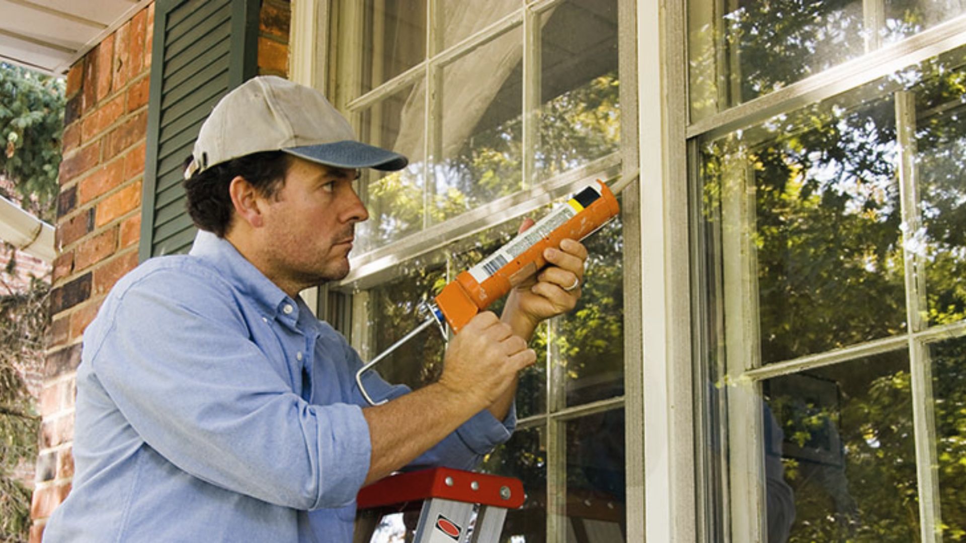 Worker applies caulk to window frame with caulking gun to seal drafts and improve insulation