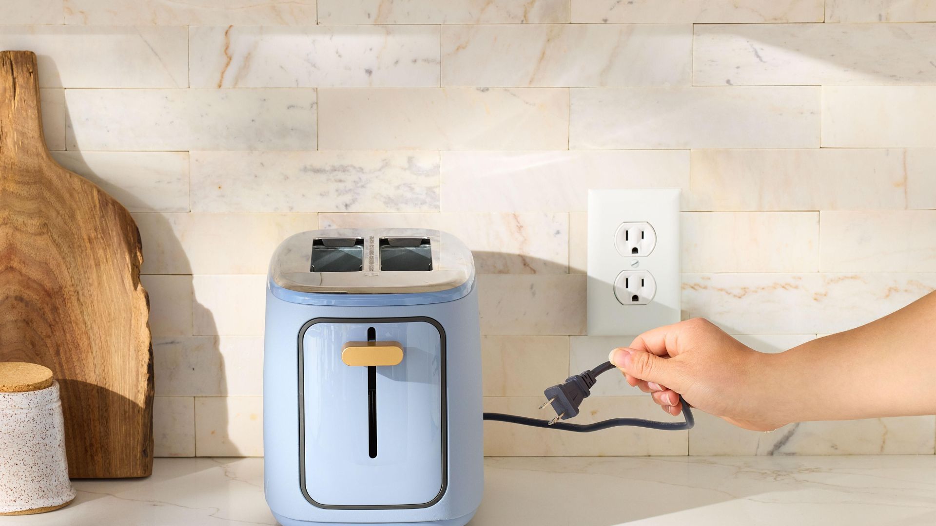 Person unplugging a light blue toaster from a kitchen outlet to prevent phantom energy use.