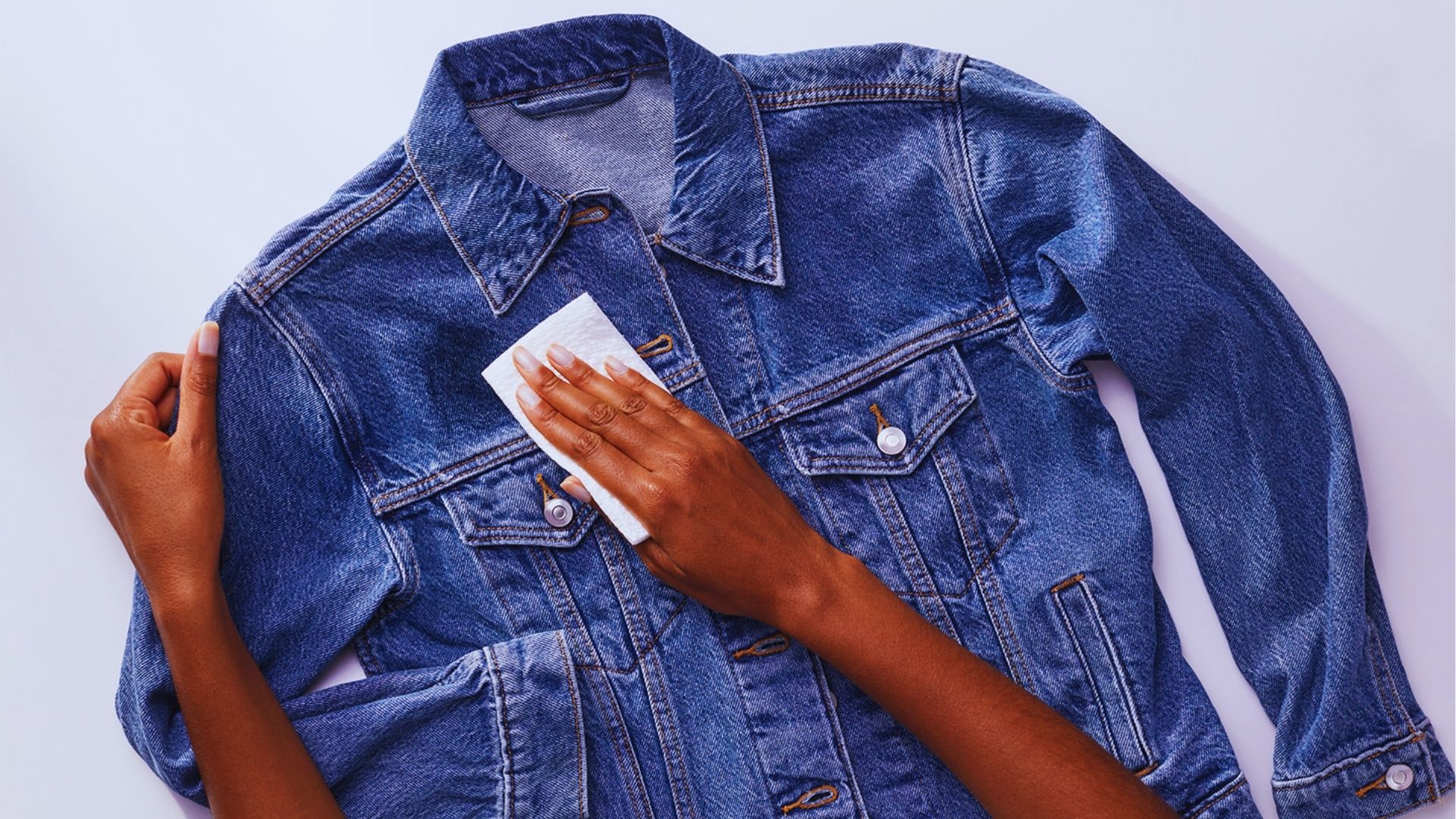 Hand blots denim jacket with paper towel to lift fresh ink stains from clothes before it sets.