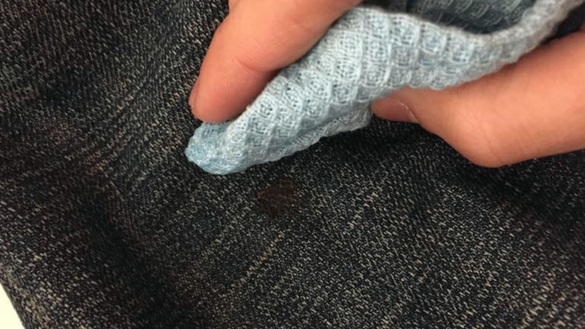 Person dabs a small stain on dark denim with a light blue cloth.