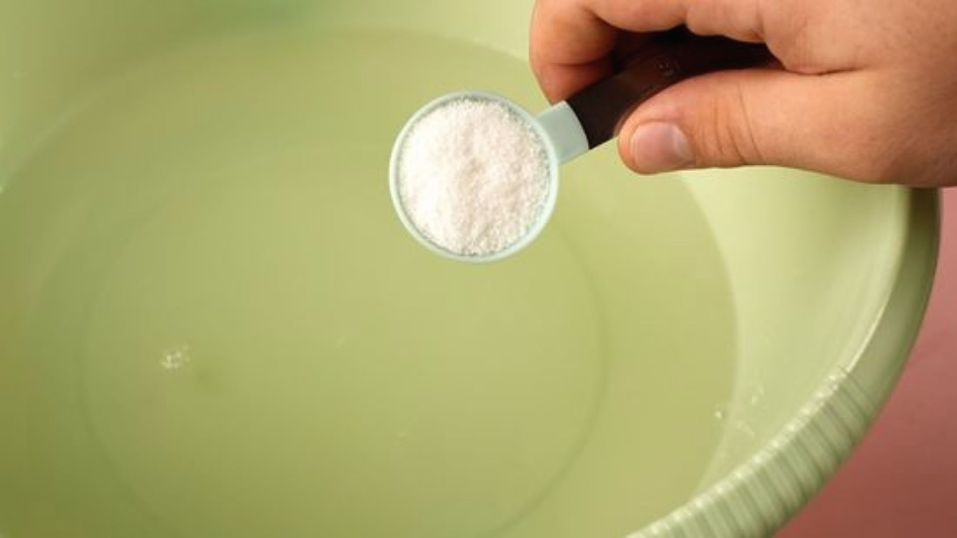 Hand pours a spoonful of white vinegar into a basin of water for pre-soaking.