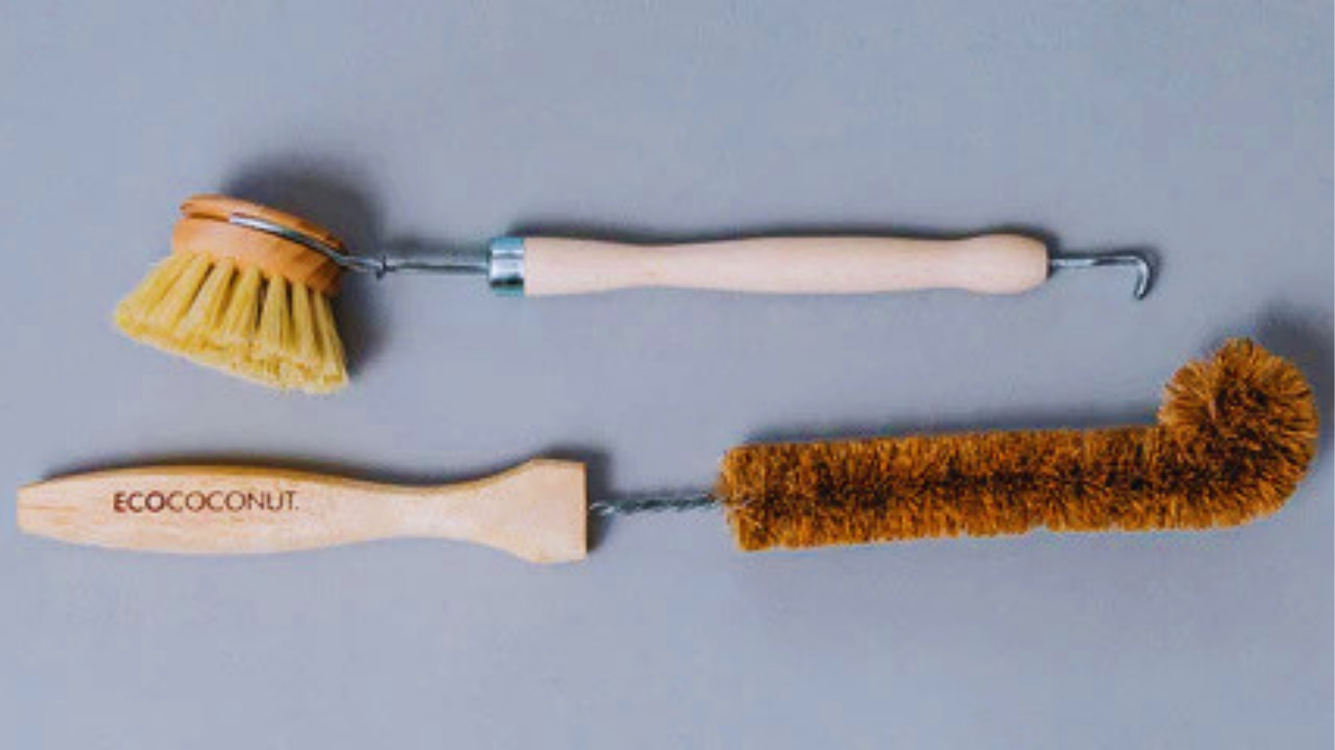 Two eco-friendly bottle cleaning brushes on gray background one dish brush with wood handle and one long brown coconut fiber brush labeled ECOCOCONUT.