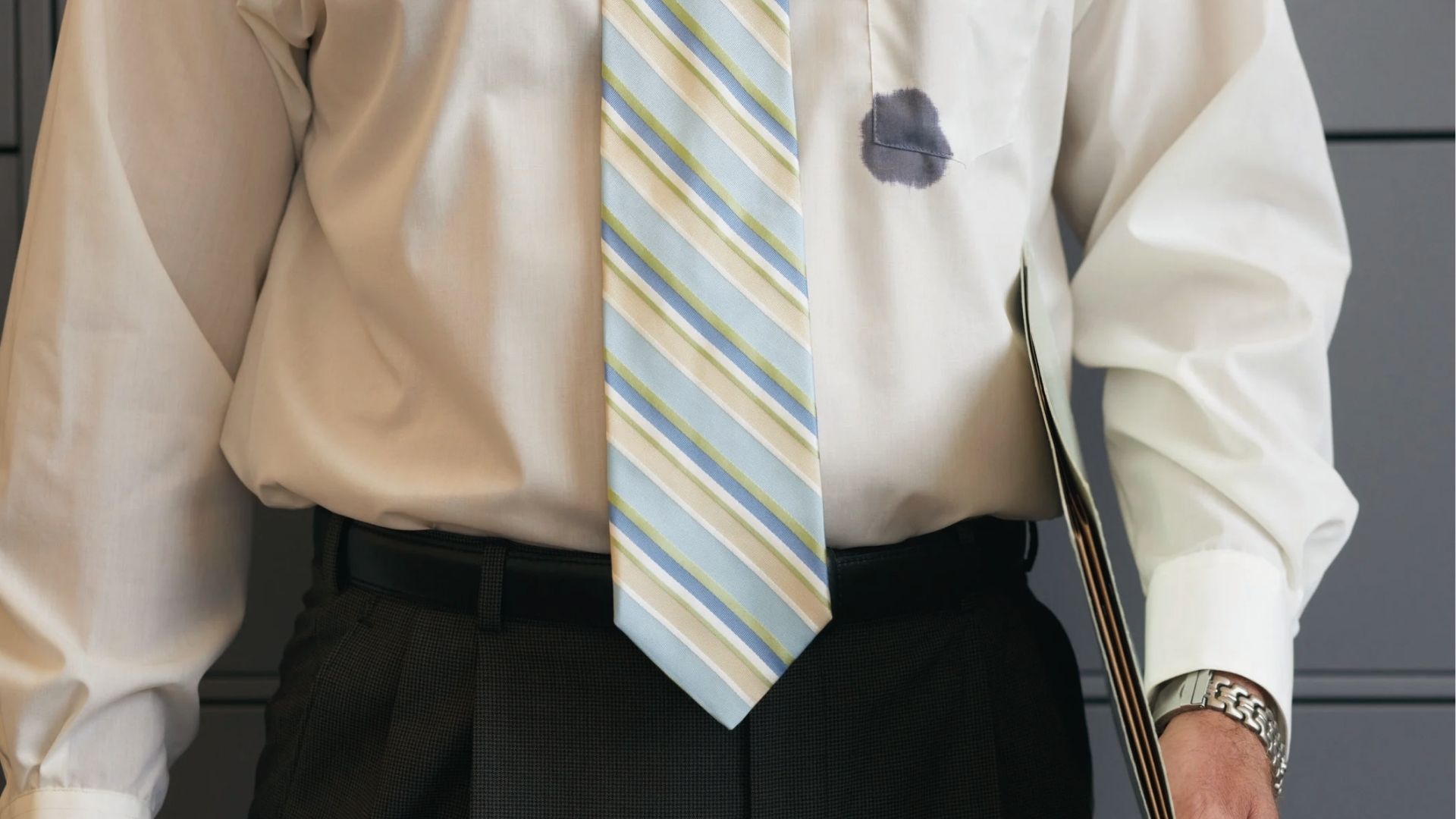 A man in an office shirt with a dark ink stain on chest pocket near a striped tie shows common ink accidents.