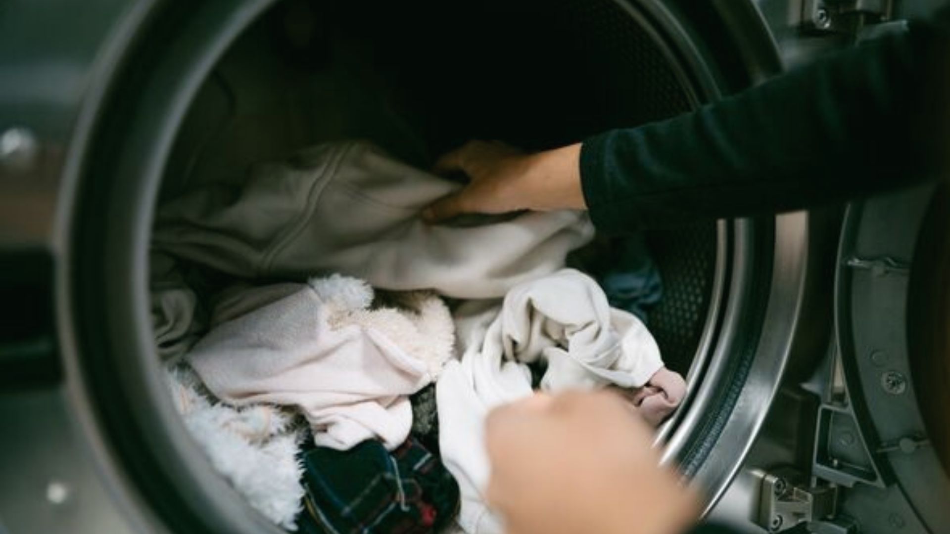 Person places clothes into a front-load washing machine, avoiding overloading.