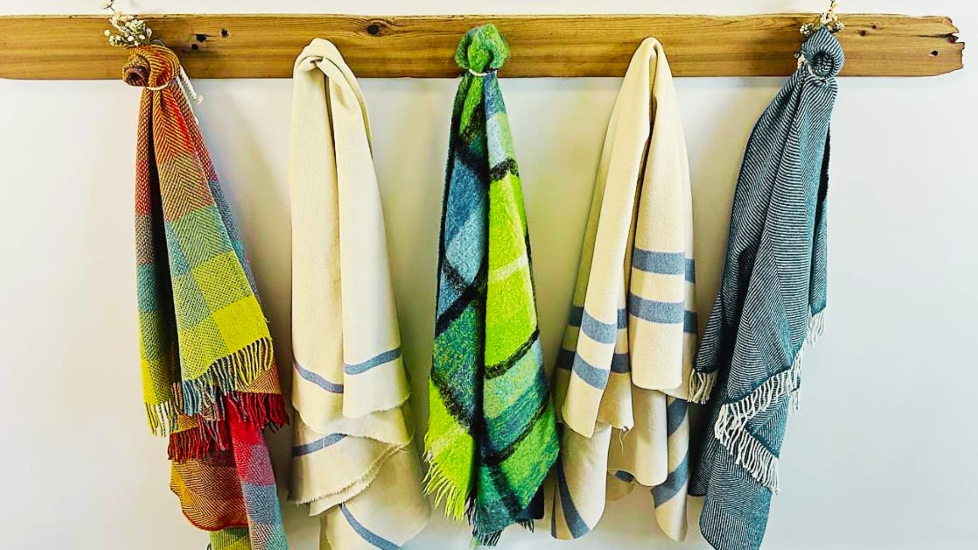 A rustic wood wall rack with hooks displaying colorful woven and striped throw blankets in a row.