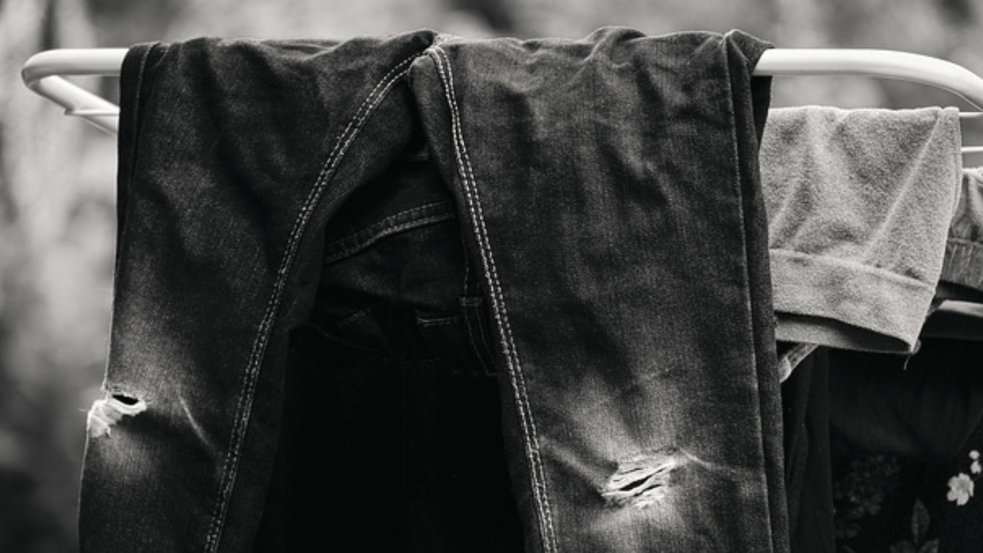 Ripped black jeans hang inside-out on a drying rack outdoors.