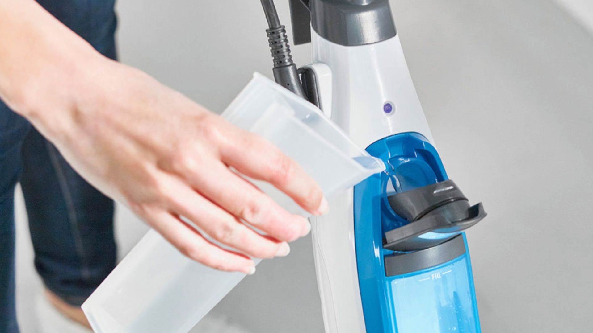 Person pouring distilled water from a container into the tank of a steam mop.
