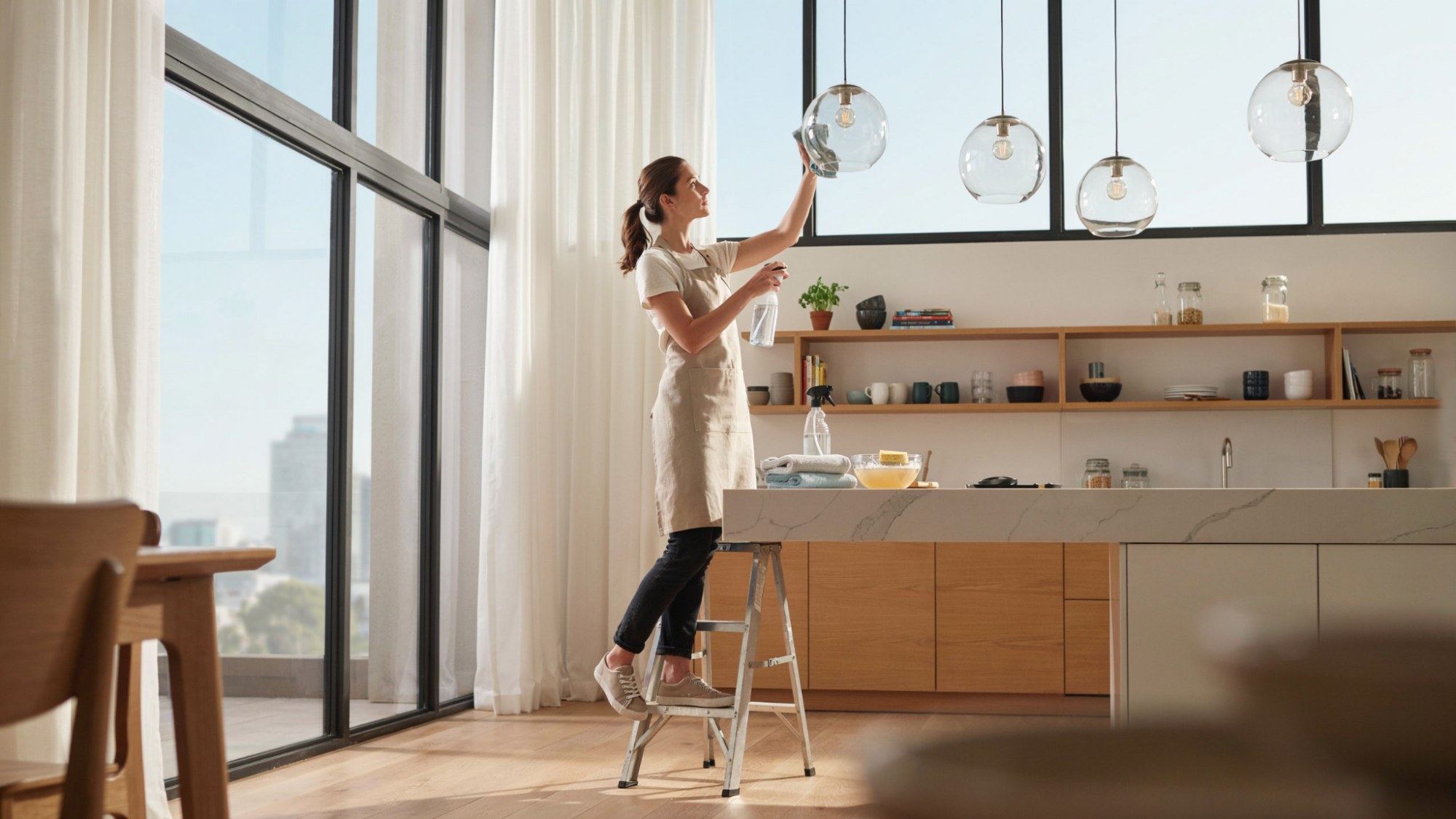 person cleaning fixed glass globe light fixture with a microfiber cloth in a bright modern kitchen