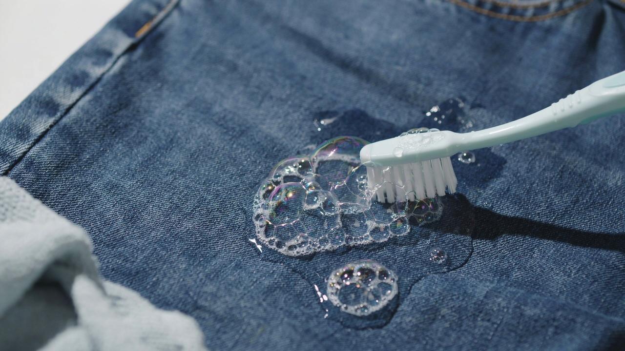 Soft toothbrush scrubbing dish soap into a slime stain on denim.