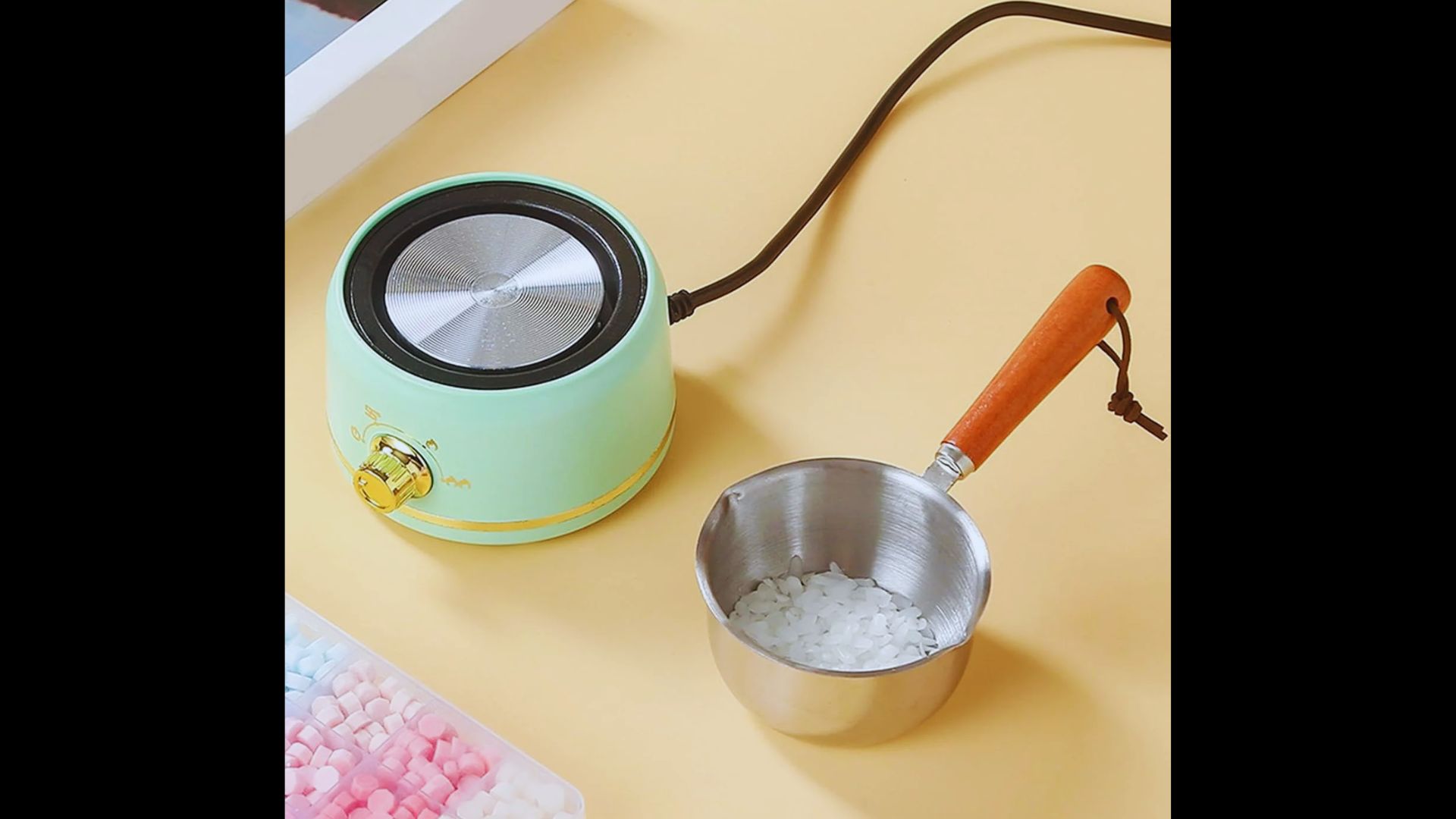 A light green electric wax warmer next to a small metal bowl filled with white wax flakes on a table.