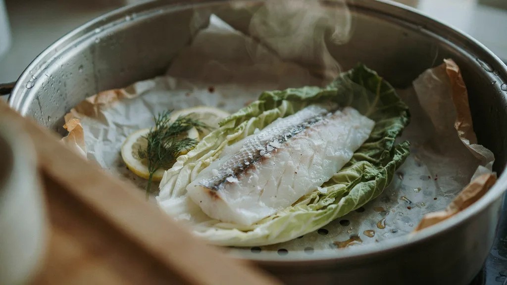 Fish placed on cabbage leaves and parchment paper for gentle steaming without sticking.