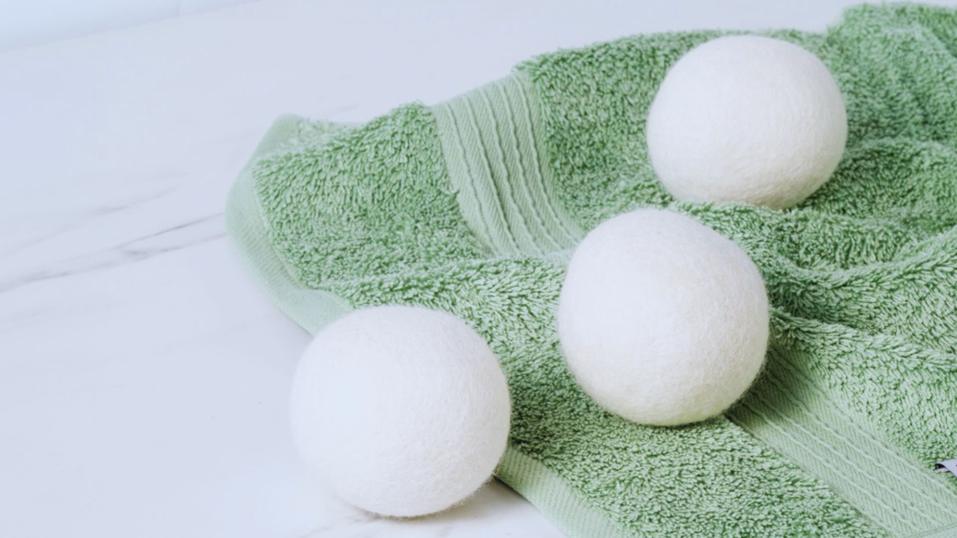 Three white wool dryer balls resting on a textured green blanket.